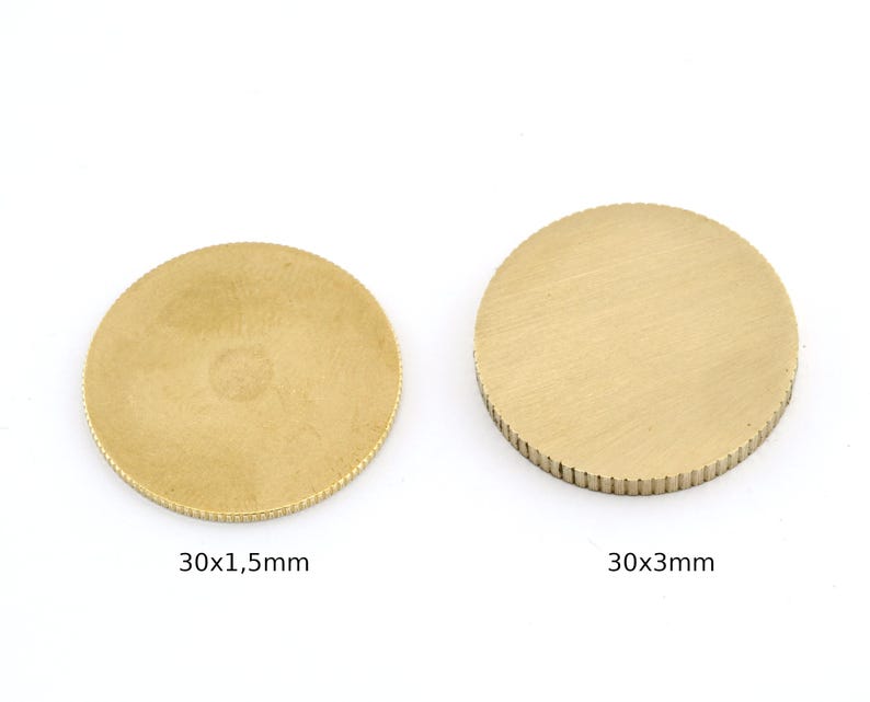 Op de afbeelding: Twee goudkleurige, ronde metalen schijven. E&eacute;n heeft een diameter van 30 mm en een dikte van 1,5 mm, de andere heeft een diameter van 30 mm en een dikte van 3 mm. Beide hebben een getextureerd oppervlak.