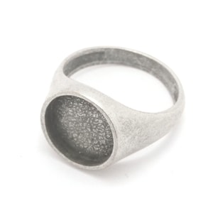 Puede incluir: Un anillo de sello de plata con un bisel redondo texturizado. El anillo está diseñado para contener un camafeo u otro elemento decorativo.