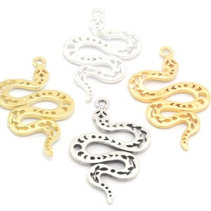 Pode incluir: Três pingentes de cobra de metal em ouro, prata e prata envelhecida. Cada pingente apresenta um design de cobra detalhado com padrões intrincados.