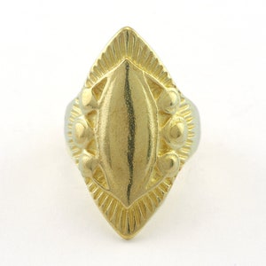 May include: A gold ring with a diamond-shaped face. The face is decorated with a raised, oval-shaped design and small, round accents.