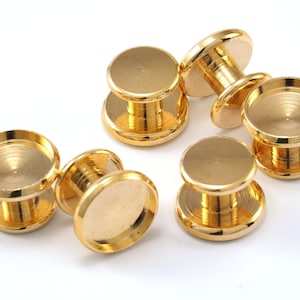 May include: Six gold-colored metal rivets with a flat top and a circular base. The rivets have a shiny, reflective surface and are arranged on a white background. The rivets are designed for jewelry making or crafting.