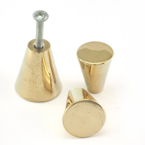 Op de afbeelding: Drie gouden kegelvormige kastknoppen met een schroef op de bovenkant van één knop.