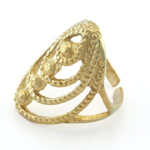 May include: A gold-colored ring with an openwork design. The ring features a series of curved lines and decorative elements, including small, textured spheres. The ring's adjustable band is visible. This piece of jewelry is suitable for everyday wear.