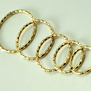 Op de afbeelding: Vijf gouden ringen met een getextureerd oppervlak. De ringen zijn op elkaar gestapeld, met de grootste ring onderaan en de kleinste ring bovenaan.