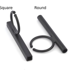 May include: Two black metal mug holders, one with a square base and one with a round base. Both holders have a circular opening for a mug.