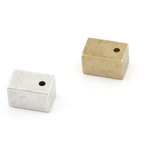 May include: Two rectangular metal beads with a hole in the centre. The bead on the left is silver and the bead on the right is gold.