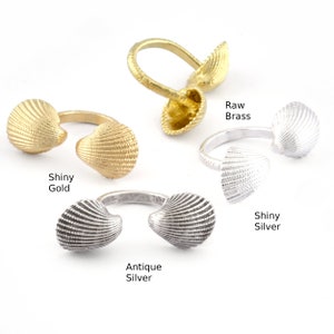 Può includere: Quattro finiture diverse di un anello a forma di conchiglia. L'anello è in metallo e ha una finitura oro lucido, argento anticato, argento lucido e ottone grezzo.