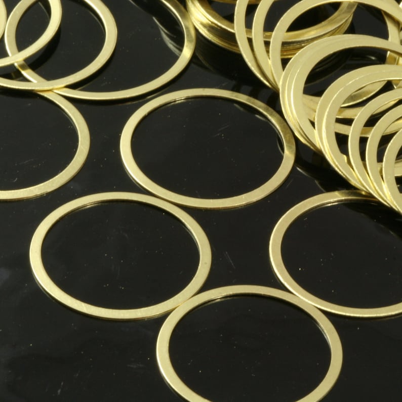 May include: A group of gold-colored metal rings, arranged in a circular pattern on a black surface. The rings are of varying sizes and are stacked on top of each other.