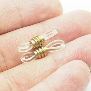 以下が含まれることがあります： 金色の金属製のアクセントが付いた透明なプラスチック製の眼鏡ホルダー2個。ホルダーは、眼鏡が耳から滑り落ちないように設計されています。