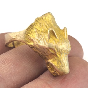 May include: A gold-colored ring with a wolf head design. The wolf's head is detailed and has a textured surface.