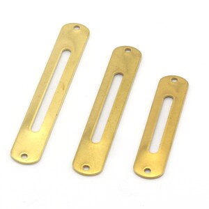 May include: Three brass metal bar buckles with a slot in the center. The buckles are different sizes.
