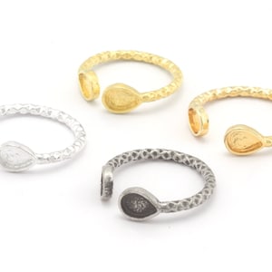 May include: Three open ring bezels with a teardrop shape. The bezels are made of metal and have a textured finish. The bezels are in gold, silver, and gunmetal.