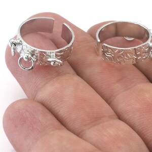 May include: Two silver rings with an open design and textured surface. Each ring has a small round charm attached to it.