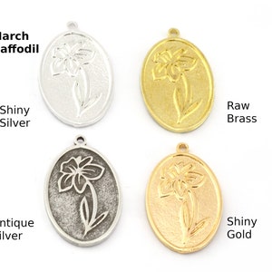 May include: Four oval-shaped metal charms with a daffodil design. The charms are in shiny silver, antique silver, raw brass, and shiny gold.