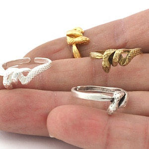 Könnte beinhalten: Drei verstellbare Ringe mit Schlangenmotiv in Silber und Gold. Die Ringe werden an den Fingern einer Person getragen.