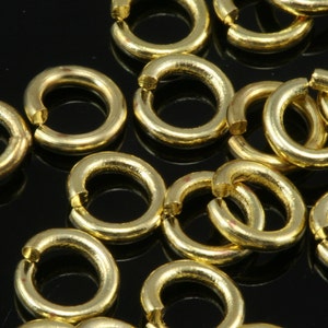 May include: A close-up of a group of gold jump rings. The rings are all the same size and are arranged in a random pattern.