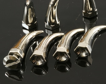 Könnte beinhalten: Sechs silberne, dekorative Schraubkappen aus Metall mit einem spitzen, hornartigen Design. Die Kappen haben eine sechseckige Basis.