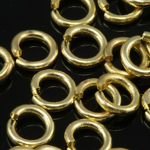 Puede incluir: Primer plano de un grupo de anillos de salto dorados. Los anillos son todos del mismo tamaño y están dispuestos en un patrón aleatorio.