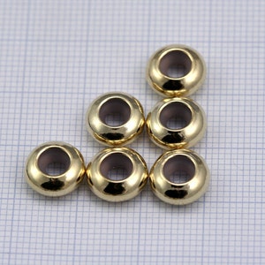 May include: Seven gold-colored metal beads with a hole in the center. The beads are arranged in a semi-circle shape.