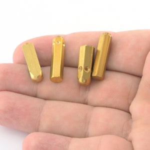 May include: Four gold-colored metal stamp punches with rounded ends, lying on a hand.