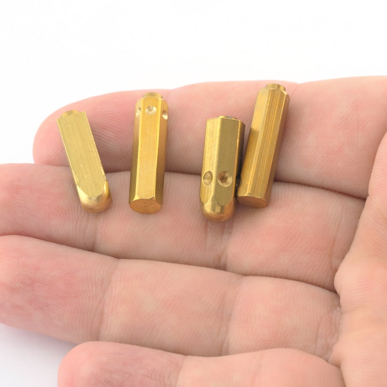 May include: Four gold-colored metal stamp punches with rounded ends, lying on a hand.