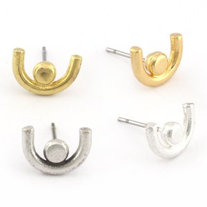 May include: Four stud earrings in gold and silver tones. Each earring features a small ball centered within a curved, U-shaped design. The posts are silver. The earrings are displayed on a white background.