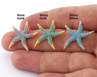 Op de afbeelding: Drie zilveren zeester-hangers met blauwe turquoise stenen. De hangers worden getoond in rosé goud, glanzend goud en glanzend zilver.