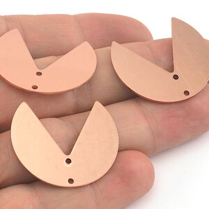 May include: Three copper-colored metal charms in the shape of a half-circle with a V-shaped cutout. Each charm has two small holes.