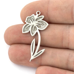 May include: Silver charm in the shape of a flower with a stem and leaves. The flower has a textured surface.