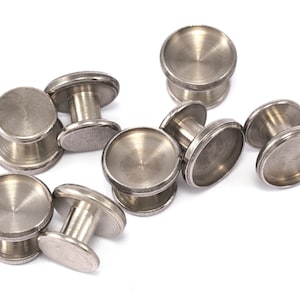 May include: A set of eight silver metal button snaps, each with a round top and a cylindrical base. The snaps are arranged in a scattered pattern on a white background.