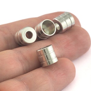 Puede incluir: Cuatro anillos de metal plateado con textura estriada. Los anillos son de diferentes tamaños y están dispuestos en una fila en una mano.