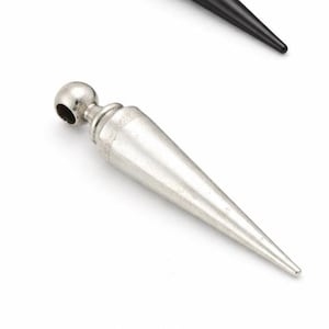 May include: A silver-colored, elongated pendant with a rounded top and a conical body. The pendant has a small hole at the top and a pointed tip. A black pendant is visible in the background.