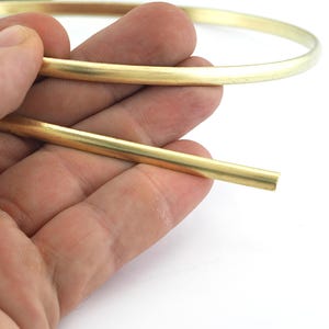 Puede incluir: Primer plano de una mano sosteniendo una pulsera de metal dorado y un trozo separado del mismo metal. La pulsera tiene un diseño simple y circular. El metal tiene un acabado brillante y pulido.