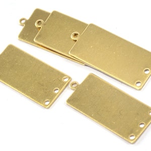 May include: Five gold-coloured metal rectangular tags with rounded corners and four holes each. The tags have a loop at the top for hanging.