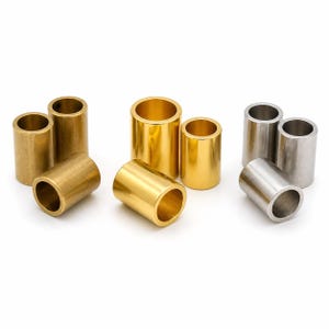 May include: A collection of cylindrical metal bushings in various sizes and finishes. The image showcases bushings in brass and silver tones, with a polished appearance. The bushings are arranged on a white surface, highlighting their metallic sheen.