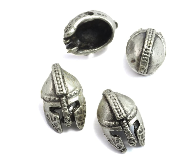May include: Four silver-toned metal helmet charms. The charms are detailed with raised lines and designs. The charms are approximately 1 inch in diameter.
