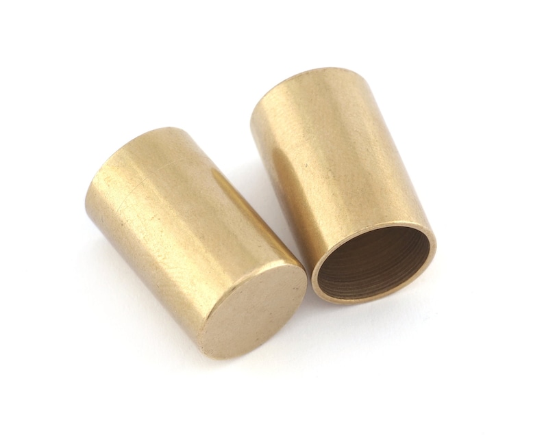 Raw brass cylindrical cord end caps with 14mm inner diameter and 25mm length on white background Two gold-colored metal cylindrical caps. The caps are smooth and have a slightly rounded edge.