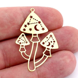 Puede incluir: Un dije de metal dorado con forma de tres setas estilizadas. Cada sombrero de seta presenta un diseño de constelación con estrellas y una luna creciente. El dije tiene un pequeño lazo en la parte superior.