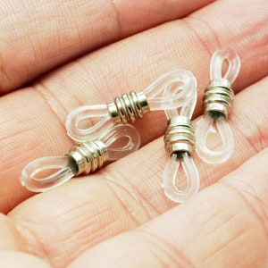 Può includere: Quattro terminali per aste di occhiali o occhiali da sole in plastica trasparente con anelli in metallo argentato. Gli anelli hanno un design rigato.