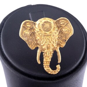 May include: A gold-colored elephant figurine with intricate details. The elephant is standing on a black circular base.