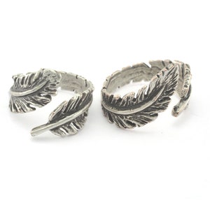 May include: Two silver adjustable rings with a feather design. The rings are open and can be adjusted to fit different finger sizes.