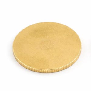 Op de afbeelding: Een ronde, goudkleurige metalen schijf met een getextureerde rand. De schijf heeft een eenvoudig ontwerp, mogelijk een munt of een decoratief element. Het oppervlak heeft een subtiele, matte afwerking. Diameter ongeveer 5 cm.