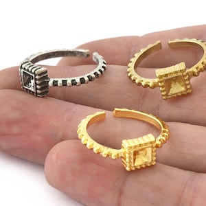 May include: Three adjustable rings with a square design. The rings are made of silver, gold, and brass. The square design has a textured border.