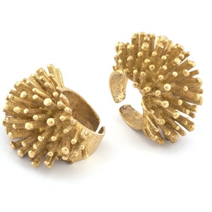 May include: Two gold-toned rings with a unique, spiky design. The rings are made of metal and have a textured surface.