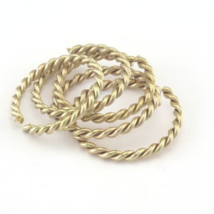 Pode incluir: Um conjunto de quatro anéis de metal torcido de cor dourada. Os anéis estão empilhados uns sobre os outros.