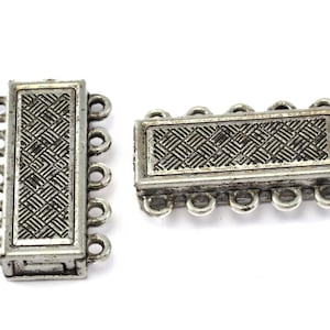 May include: Two silver-toned magnetic jewelry clasps. Each clasp has a rectangular shape with a woven pattern in the center and multiple loops for attaching jewelry. The clasps are designed to connect and secure necklaces or bracelets.