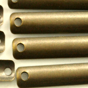 Puede incluir: Seis conectores de barra de metal dorado antiguo con agujeros en cada extremo. Los conectores están dispuestos en una fila, con los agujeros mirando al espectador.