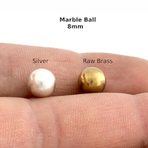 Pode incluir: Duas bolas de mármore de 8 mm, uma prateada e outra de latão bruto.