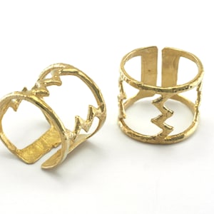 May include: Two gold-toned rings with a zig-zag pattern. The rings are open and can be adjusted to fit different finger sizes.
