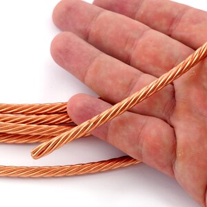 May include: A close-up of a bundle of copper wire, twisted together. The wire is a bright, shiny copper colour and is lying on a white surface.